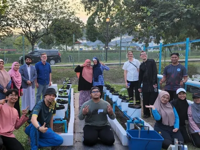 The farm team and guests posing among raised planting beds and aquaponics tanks at dusk